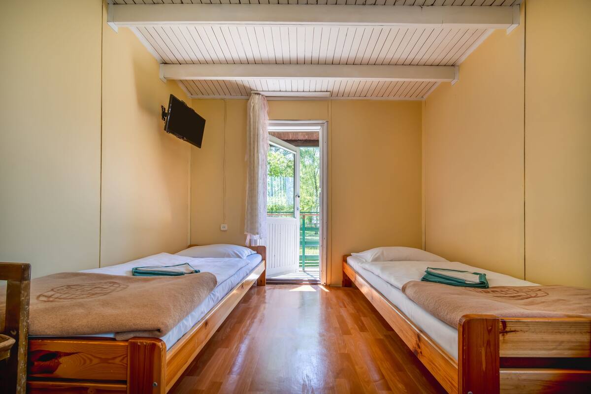 A room with two wooden beds, a television mounted on the wall, and a door leading to an outdoor area.
