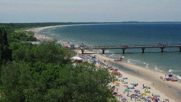 A beach with a pier, beach umbrellas, and people.