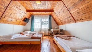 A room with wooden ceilings and floors, two beds, a desk, and a window with curtains.