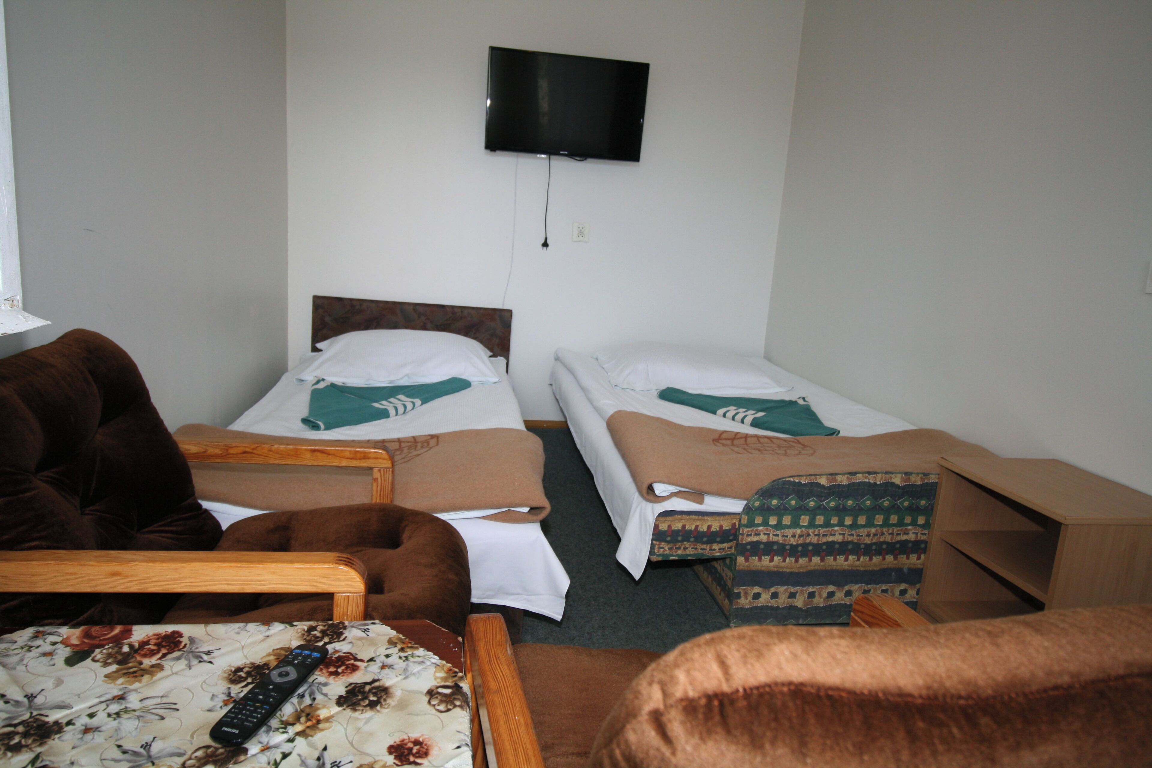 Een hotelkamer met twee eenpersoonsbedden, een slaapbank, een kleine tafel en een aan de muur bevestigde televisie.