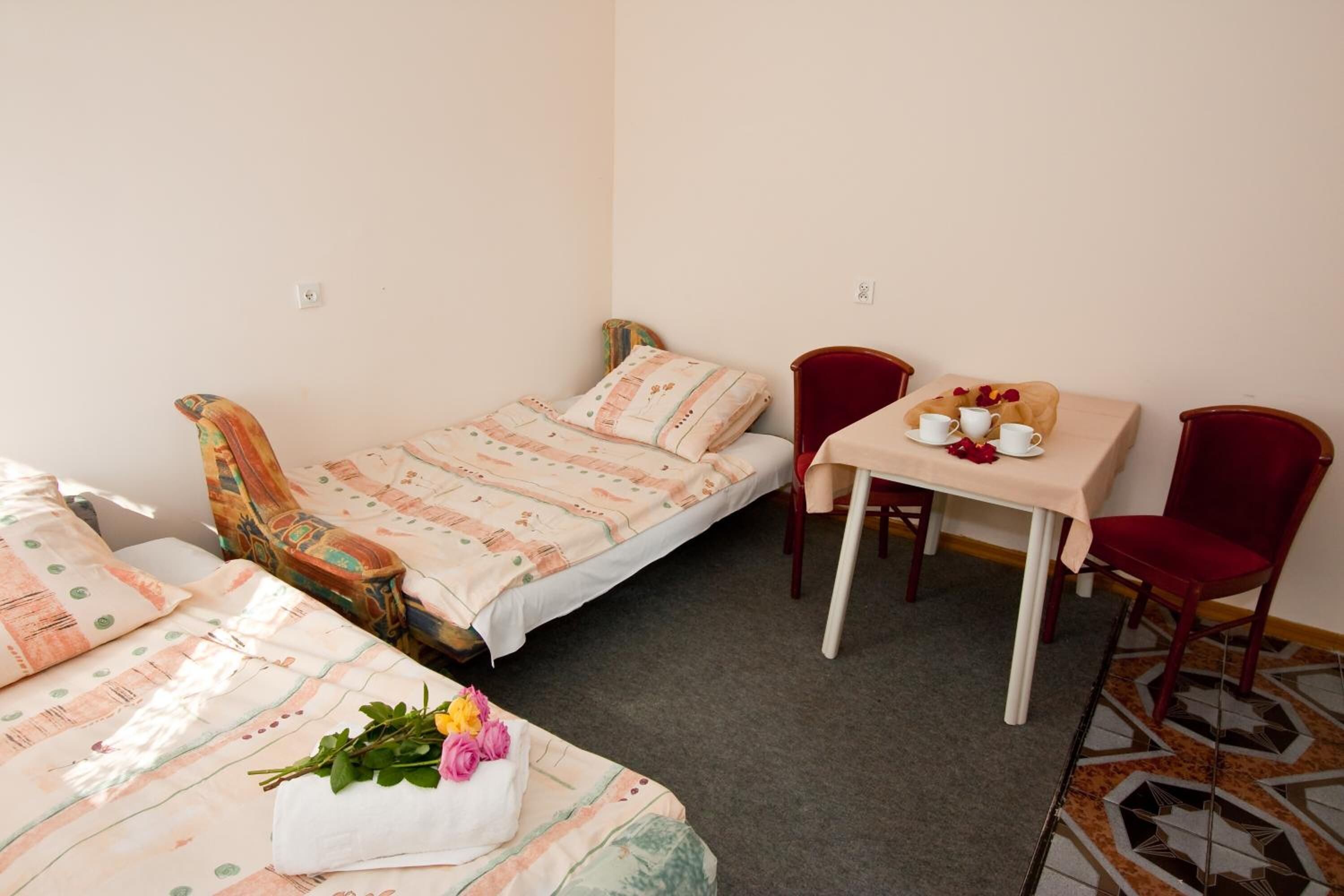 A small, cozy room with a single bed, a small table with a chair, and a decorative pillow.