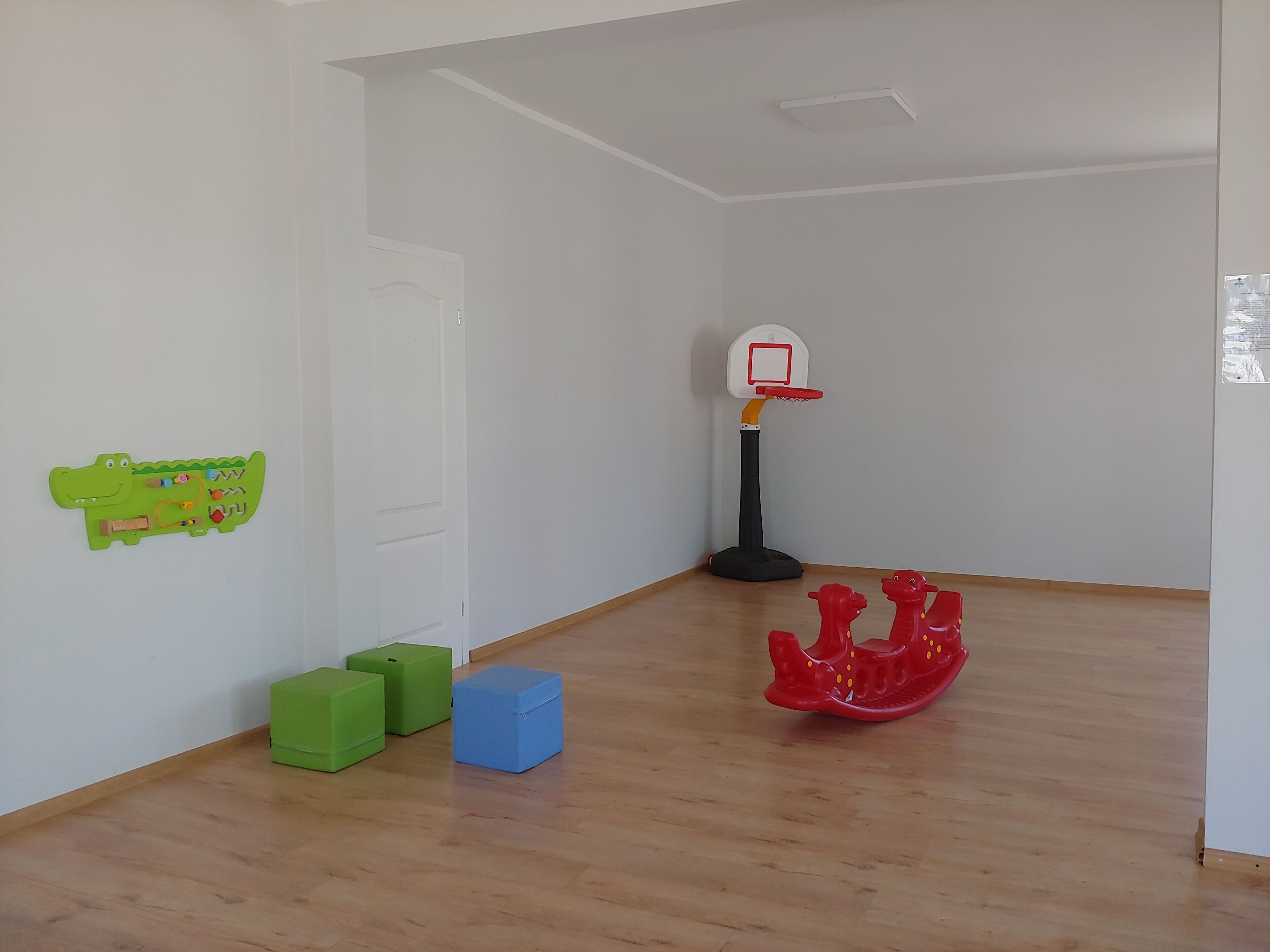 Une pièce avec un panier de basket, des boîtes de rangement vertes et bleues, et un cheval à bascule rouge.