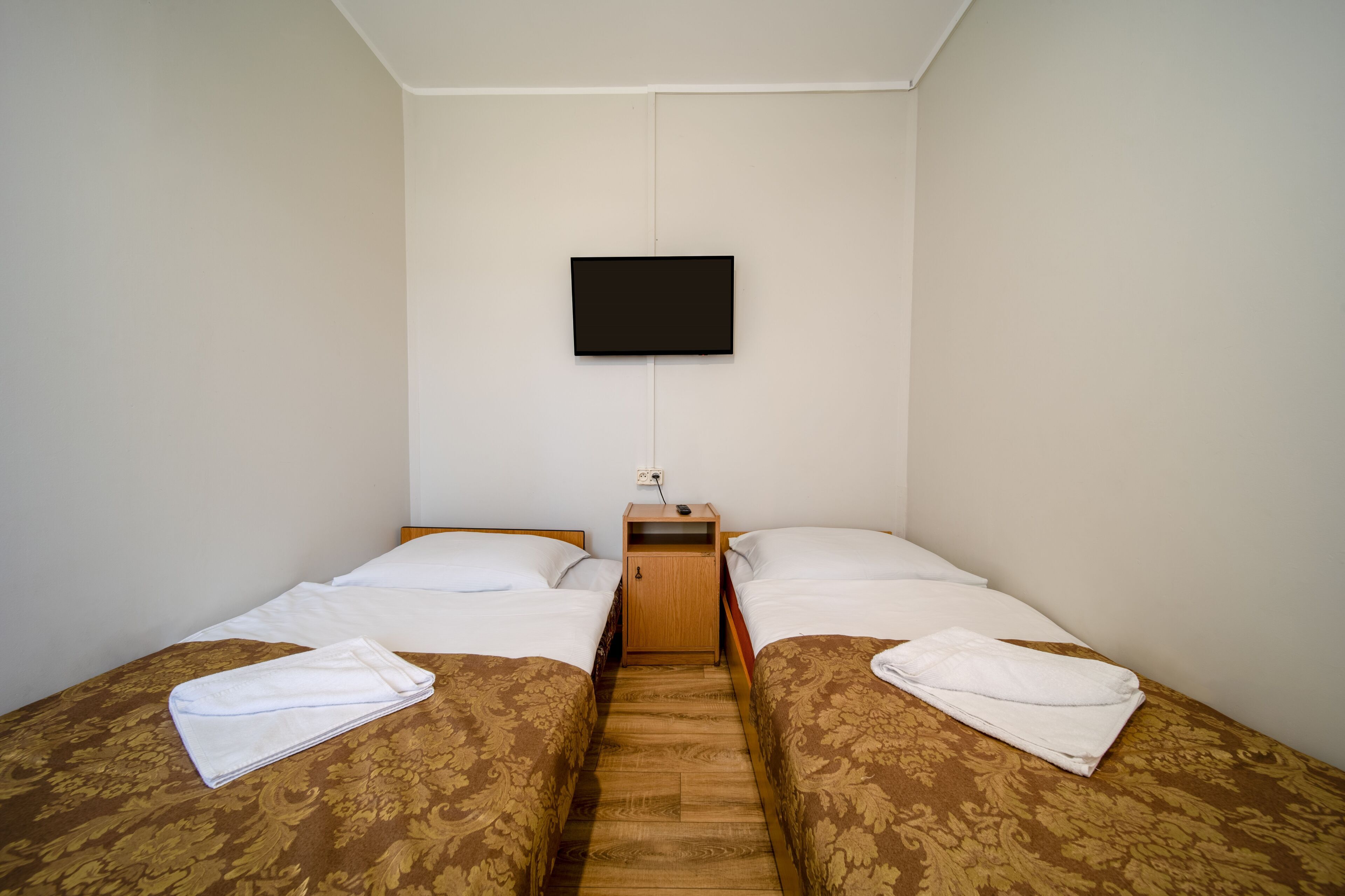 Une chambre double avec deux lits, un téléviseur fixé au mur et une table de chevet en bois.
