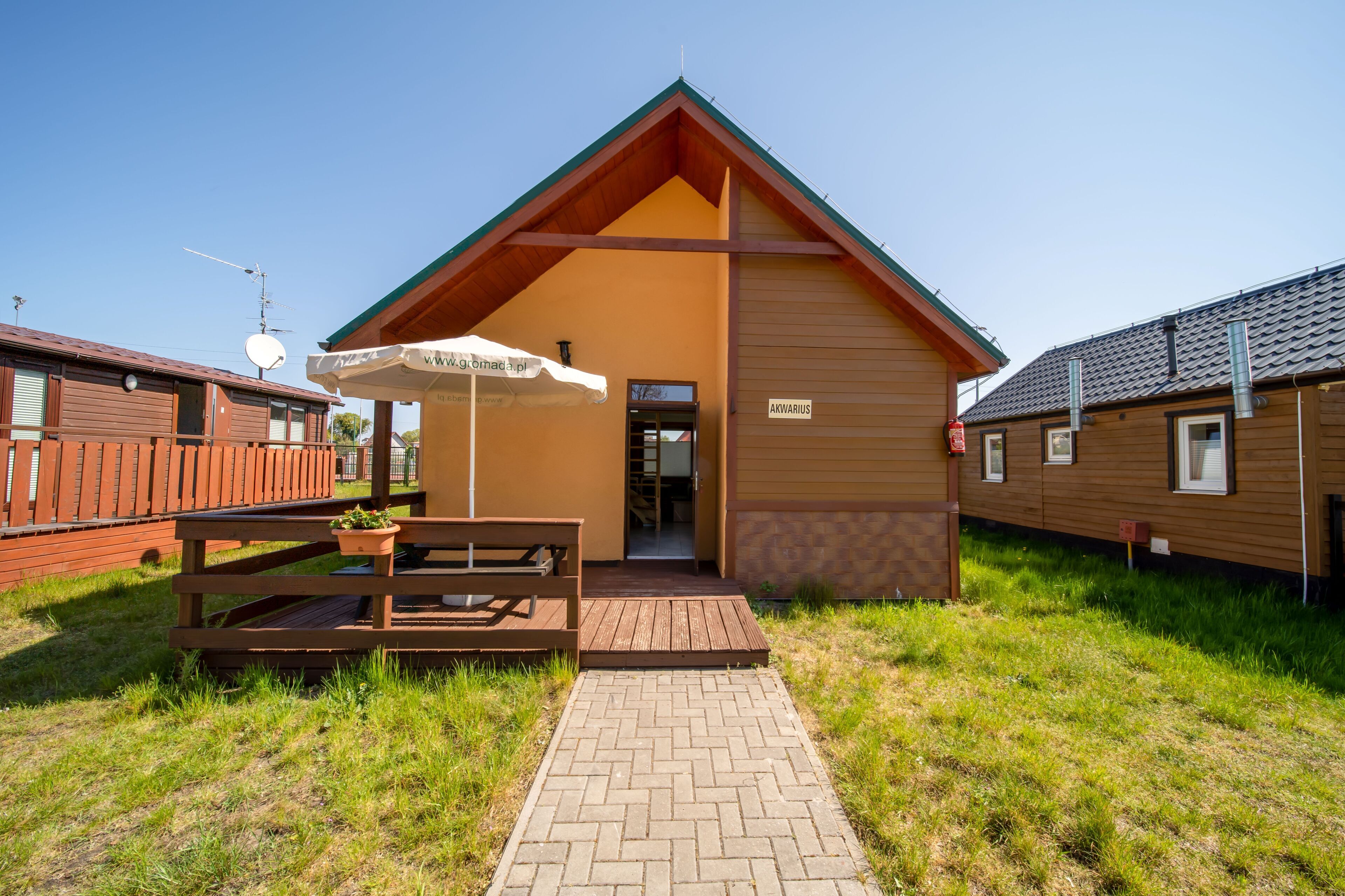A wooden building with a pitched roof, a sign reading "AKWARIUS," and a picnic table with a white umbrella.