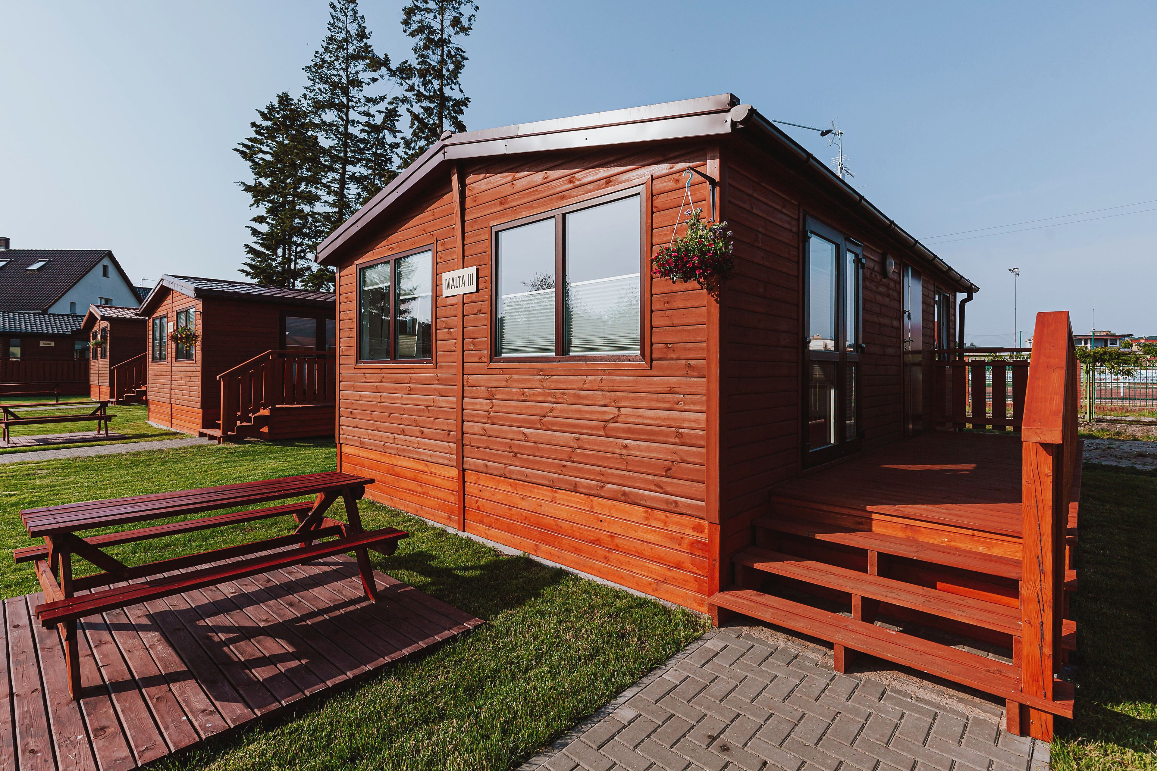 A wooden cabin with a sign reading "Malta III," a wooden deck, and a picnic table.
