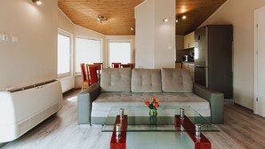 A modern living room with a beige sofa, a glass coffee table, and a kitchen in the background. - OW Gromada Apartamenty (Miedzyzdroje)