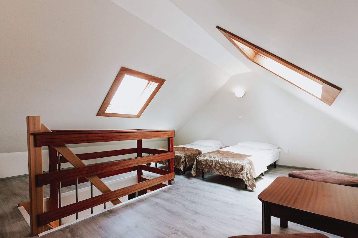 Ein Zimmer mit schrägem Dach, einer hölzernen Bank, zwei Betten mit weißer Bettwäsche und einem Tisch.