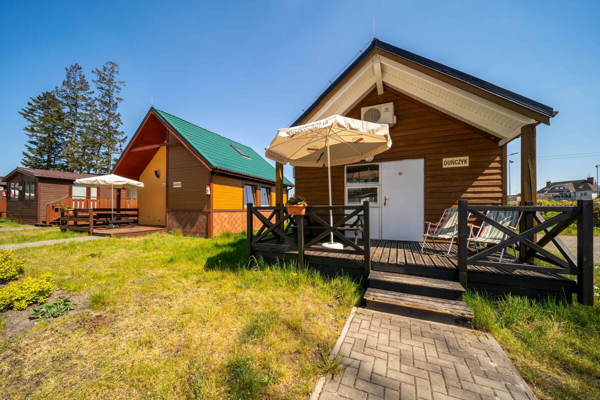 Eine Holzhütte mit grüner Dachdeckung, einer überdachten Sitzgruppe im Freien und einem Schild mit der Aufschrift 'DUNCZYK'.