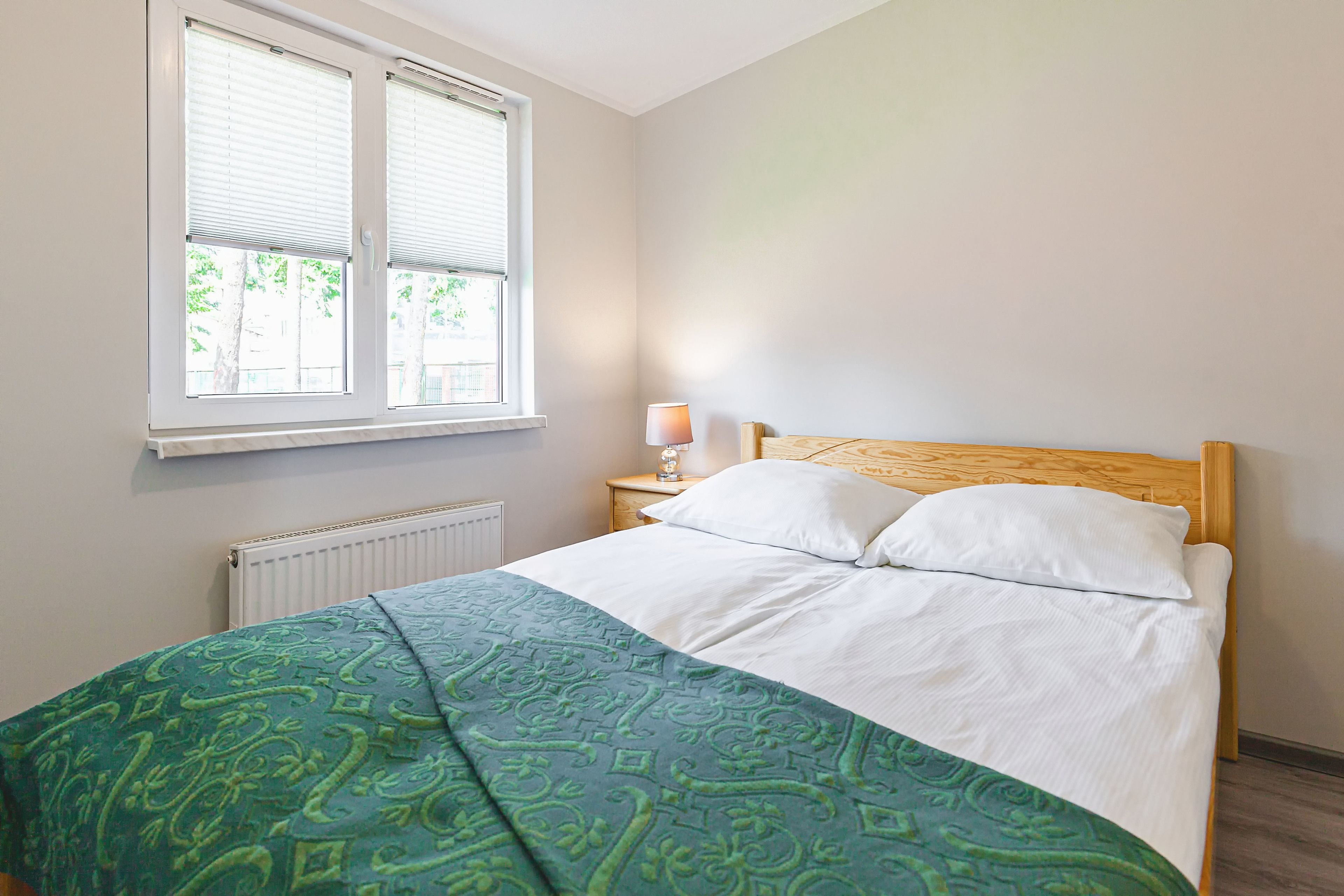 Un dormitorio con cama, ventana, mesita de noche y lámpara.