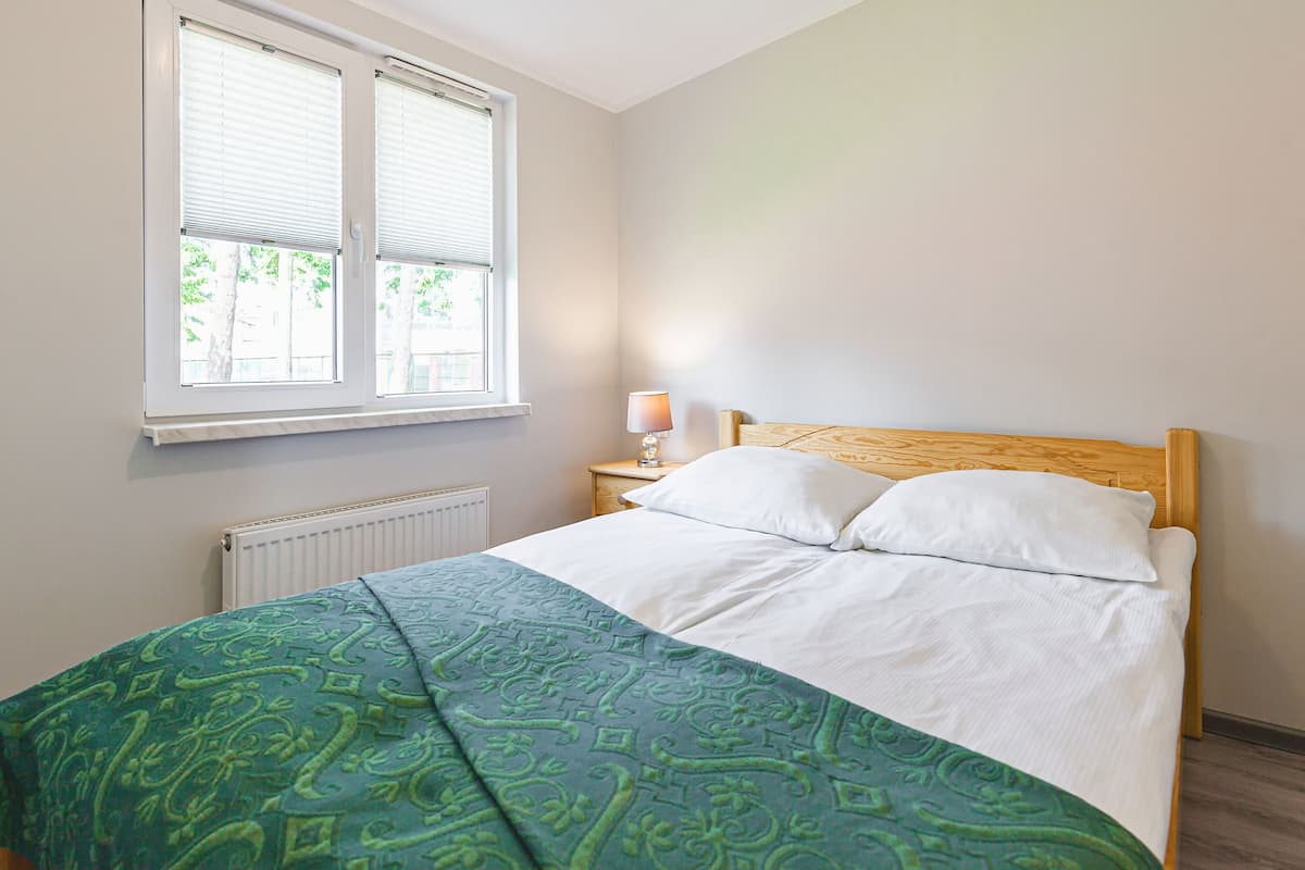 Ein Schlafzimmer mit Bett, Fenster, Nachttisch und Lampe.