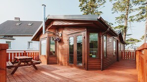 A wooden deck with a picnic table, a covered area with glass doors, and a chimney. - OW Gromada Apartamenty (Miedzyzdroje)