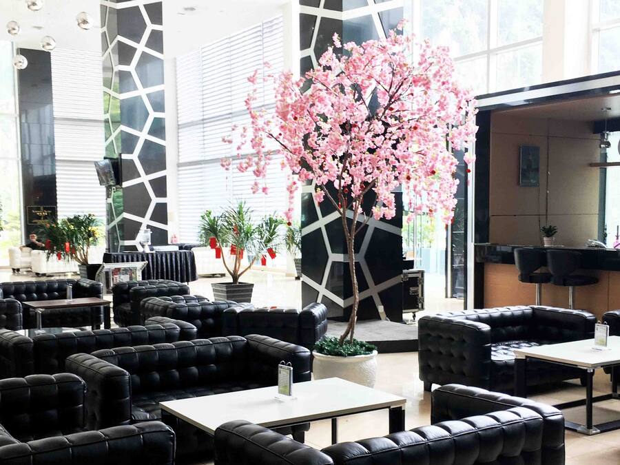 A modern lounge area with black leather sofas and tables, a large artificial cherry blossom tree, and a bar area with kitchenware on display.