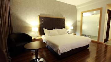 A hotel room with a large bed, two bedside lamps, a round table, a chair, and a wardrobe.