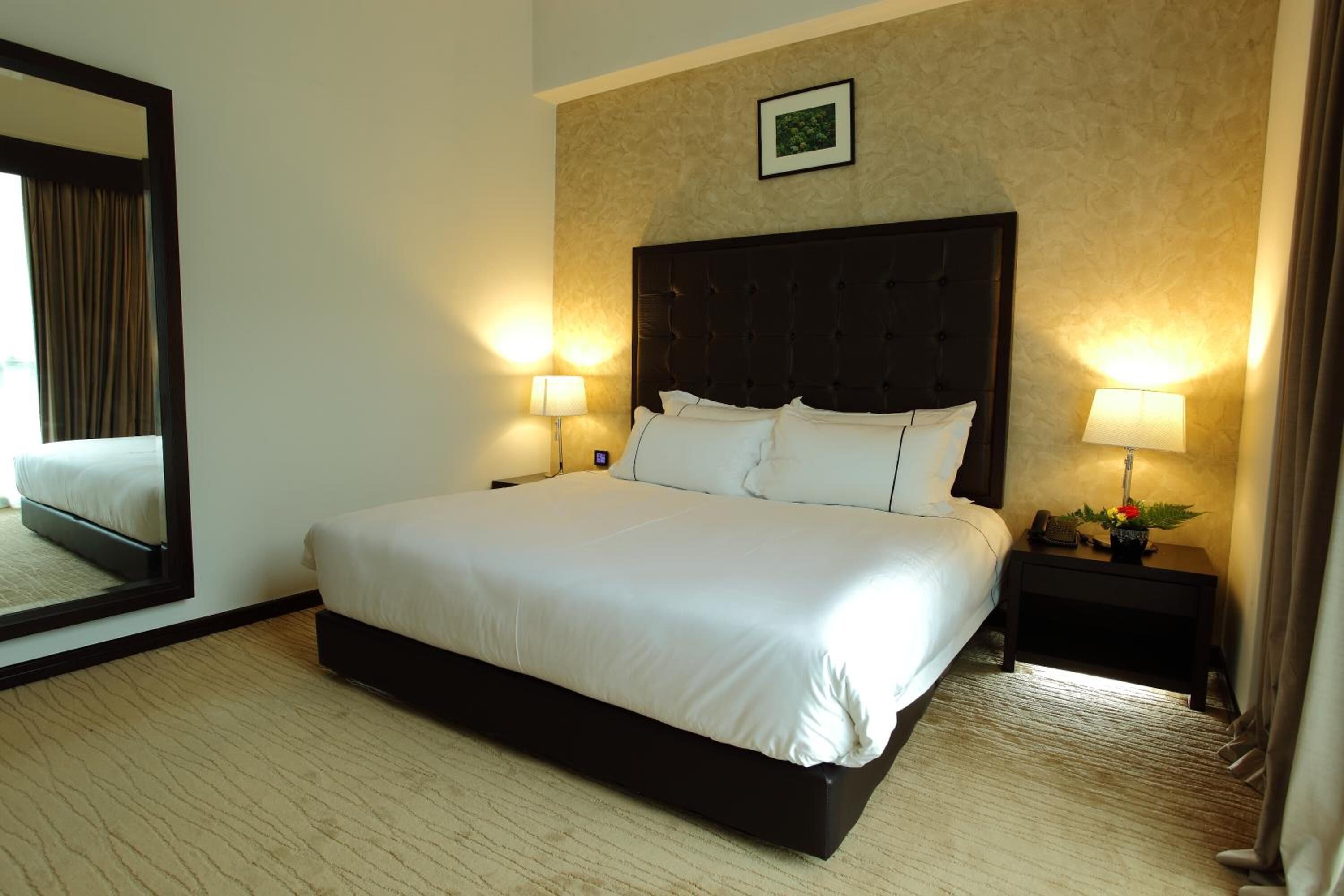 Una habitación de hotel con una cama grande, dos mesitas de noche con lámparas, un espejo y un cuadro enmarcado en la pared.