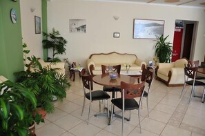 A living room with a beige sofa, a dining table with chairs, and various potted plants.