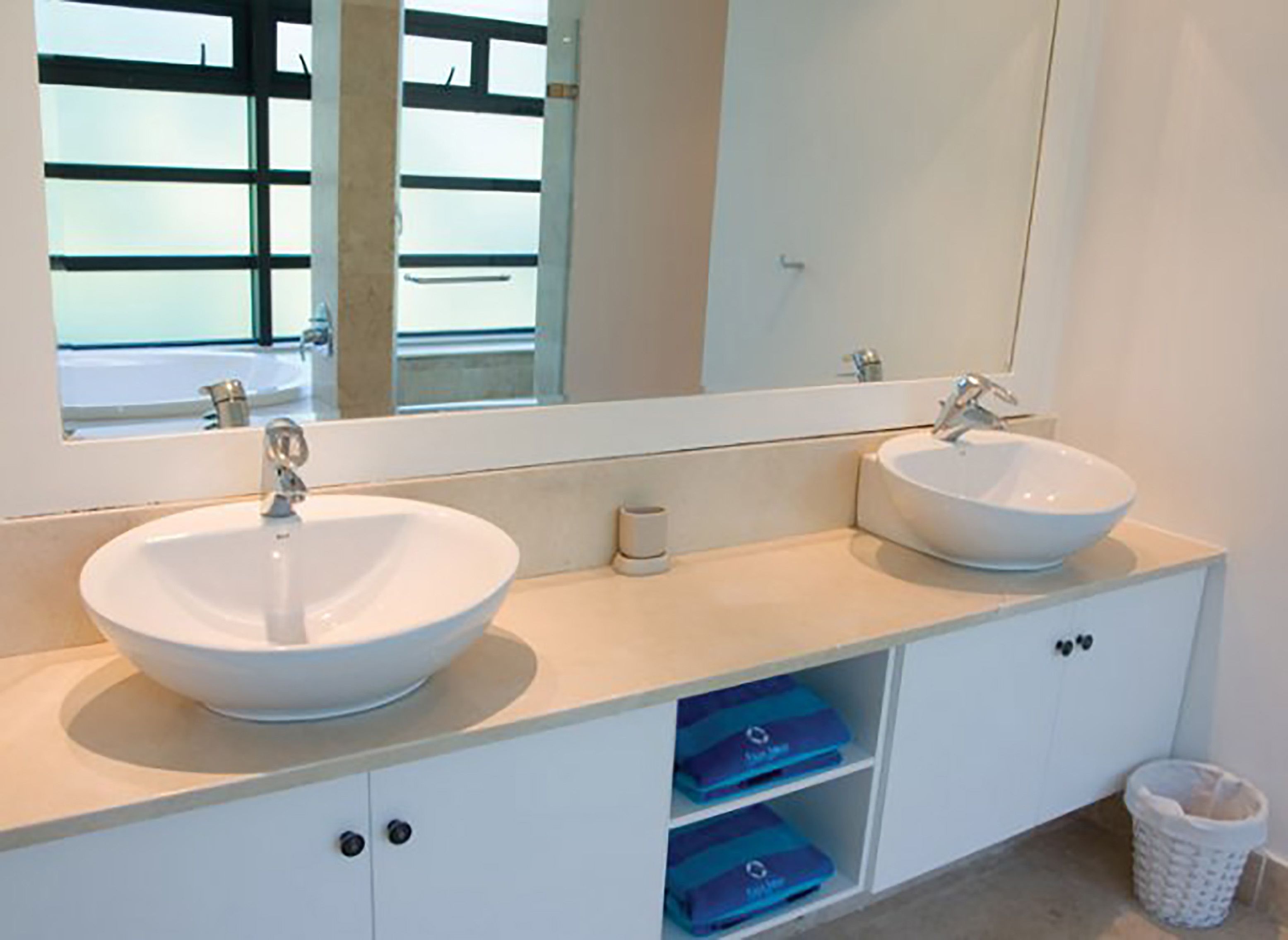 A bathroom with two white sinks, a large mirror, and a white cabinet with blue storage drawers.