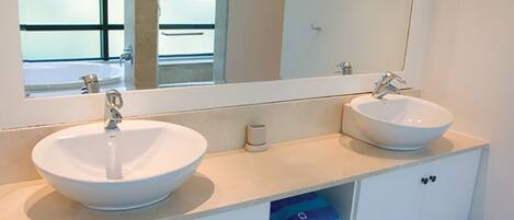 A bathroom with two white sinks, a large mirror, and a white cabinet with blue storage drawers.