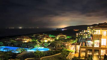 A resort with multiple bungalow-style buildings, a swimming pool, and a view of the ocean at night.