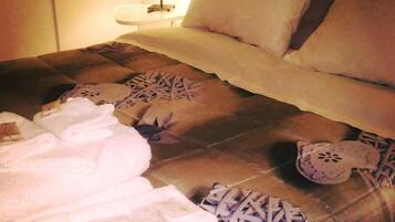 A neatly made bed with a patterned bedspread, a bedside lamp, and a small table with a lamp.