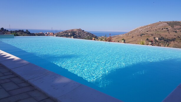 Una piscina infinita azul cristalina con vistas al mar y colinas al fondo.
