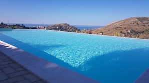 A clear blue infinity pool with a view of the sea and hills in the background. - B&B A Robba de Pupi (Agrigento)