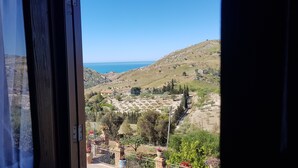 Vista desde una ventana con un cerro y un cielo azul despejado, y una masa de agua al fondo.