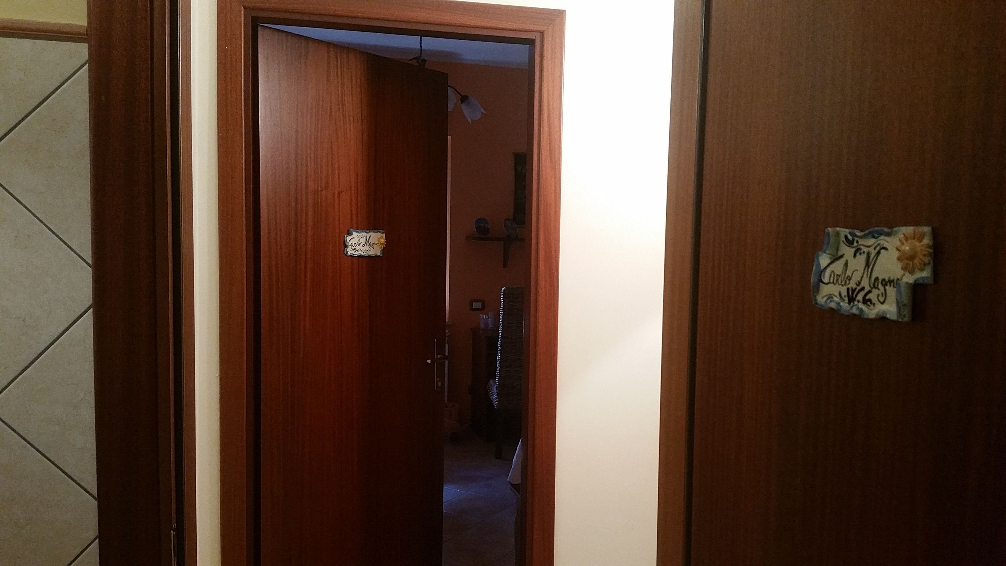 A wooden door with a nameplate, a hallway with a tiled floor, and a small shelf with decorative items.