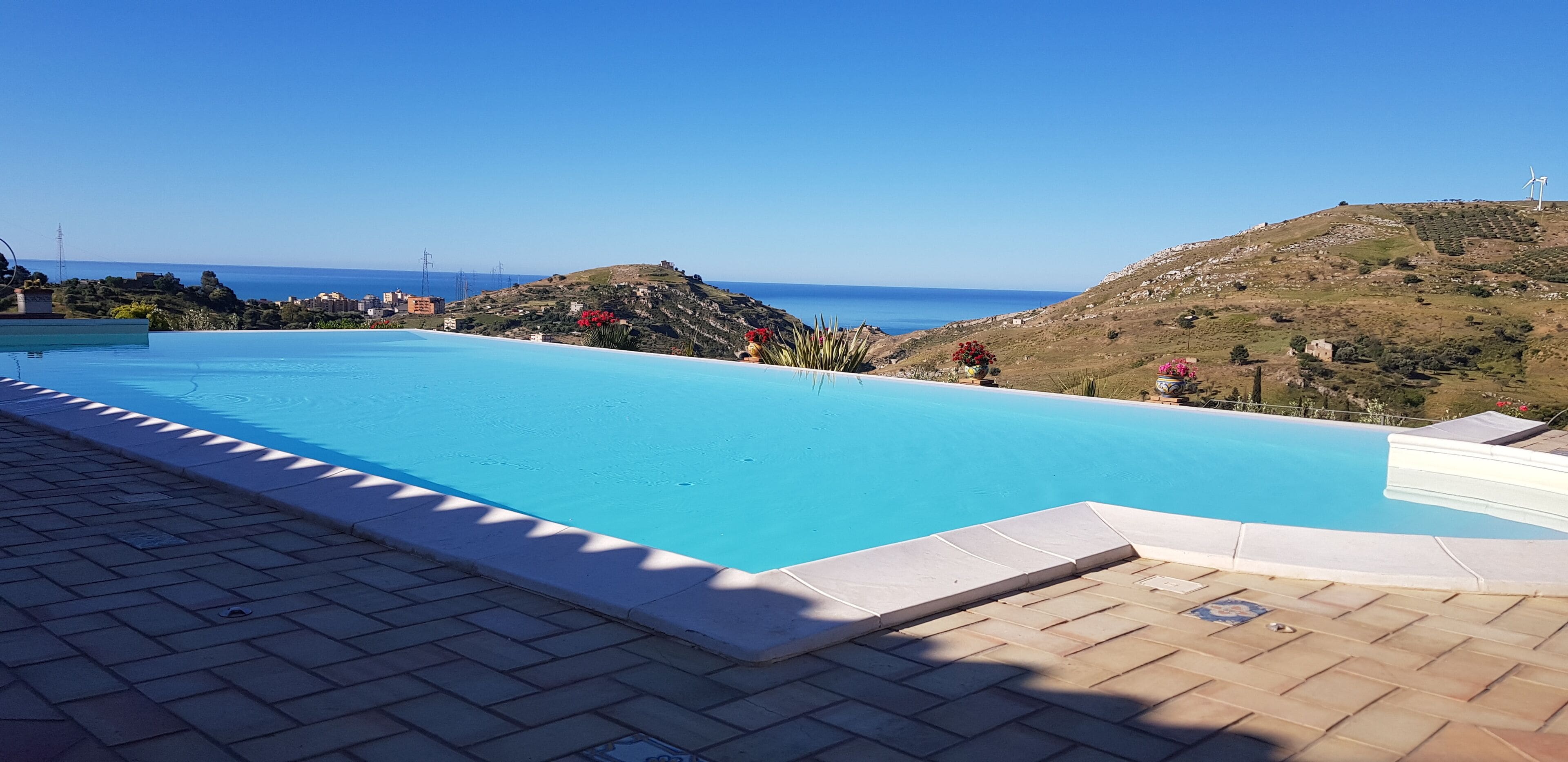 A swimming pool with a clear view of the sea and hills in the background.