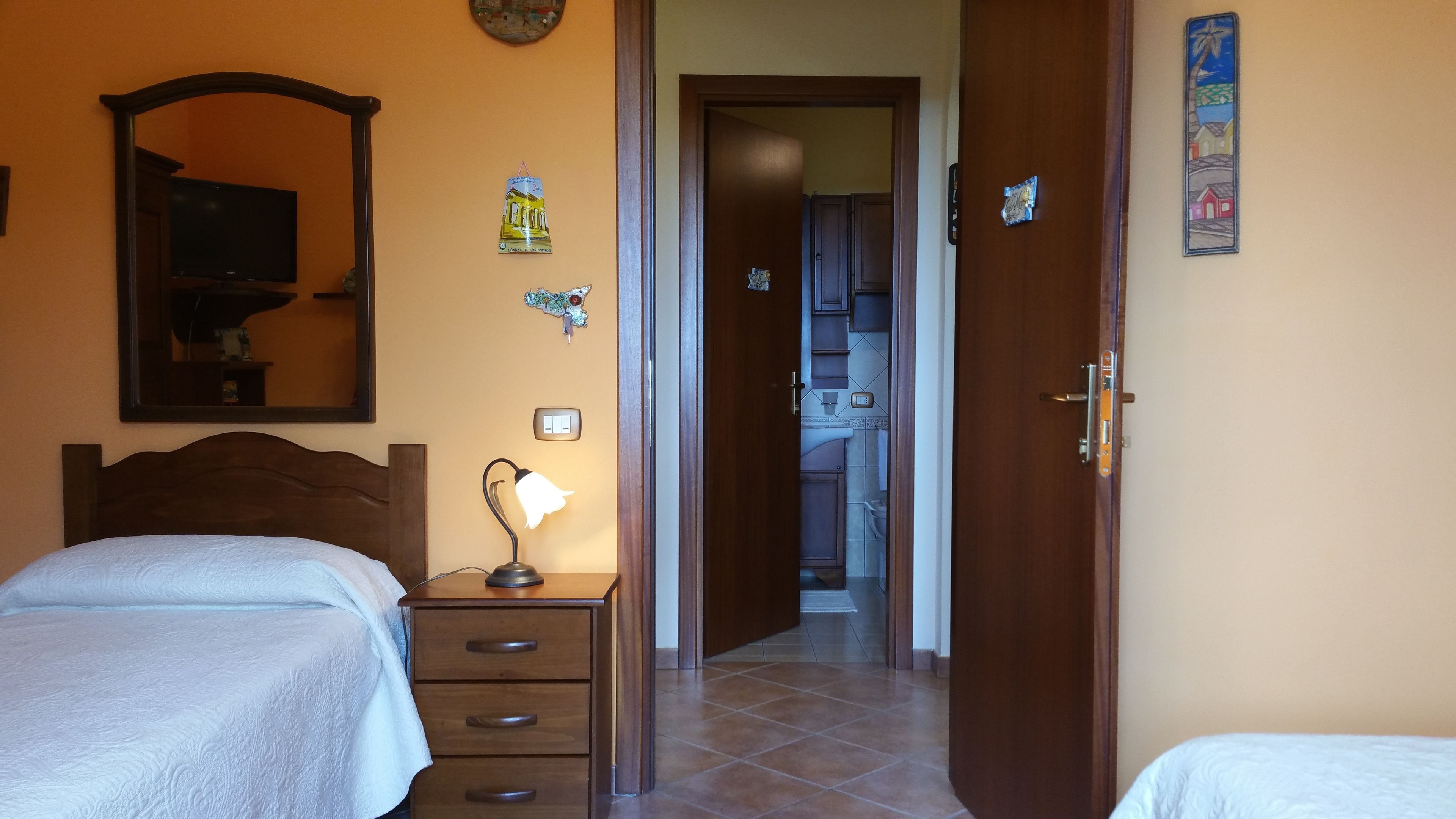 Une chambre d’hôtel avec deux lits, une table de chevet avec une lampe, un miroir et une porte donnant sur une salle de bain.
