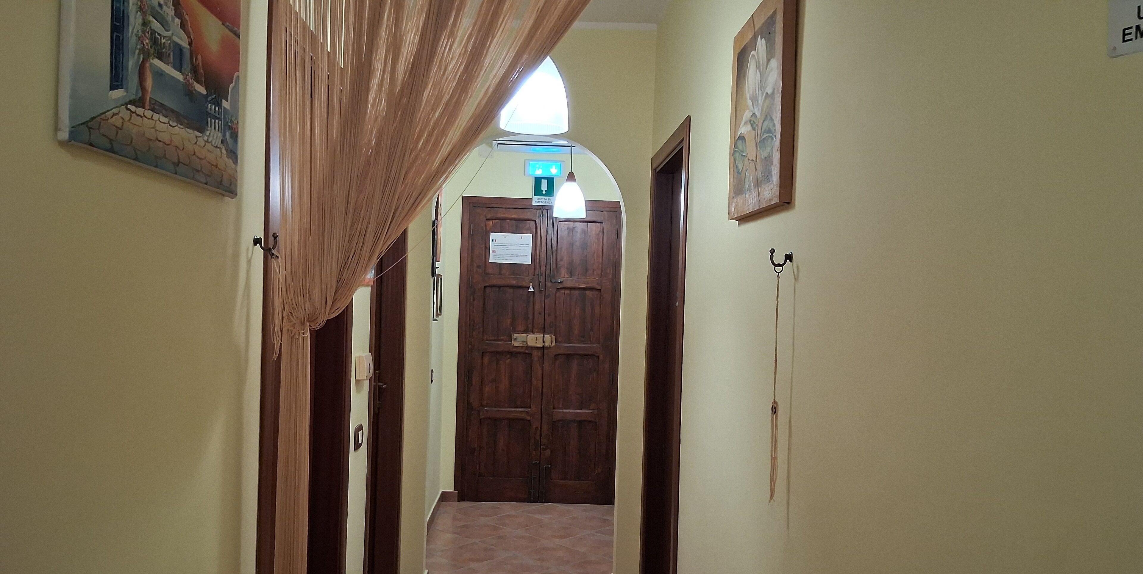Un corridoio con una porta in legno alla fine, un lampadario sopra e un quadro appeso al muro.
