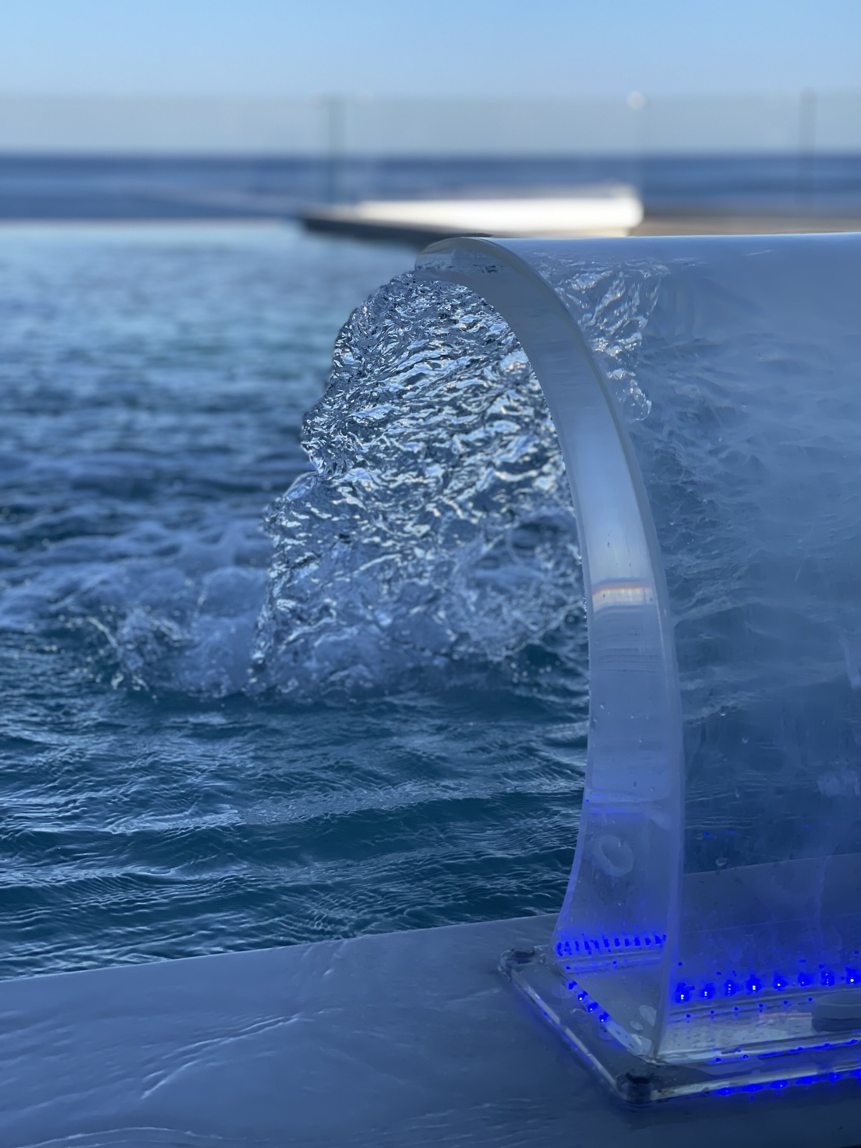 A clear view of a ship's bow cutting through the water, with a visible structure and blue lights on the deck.