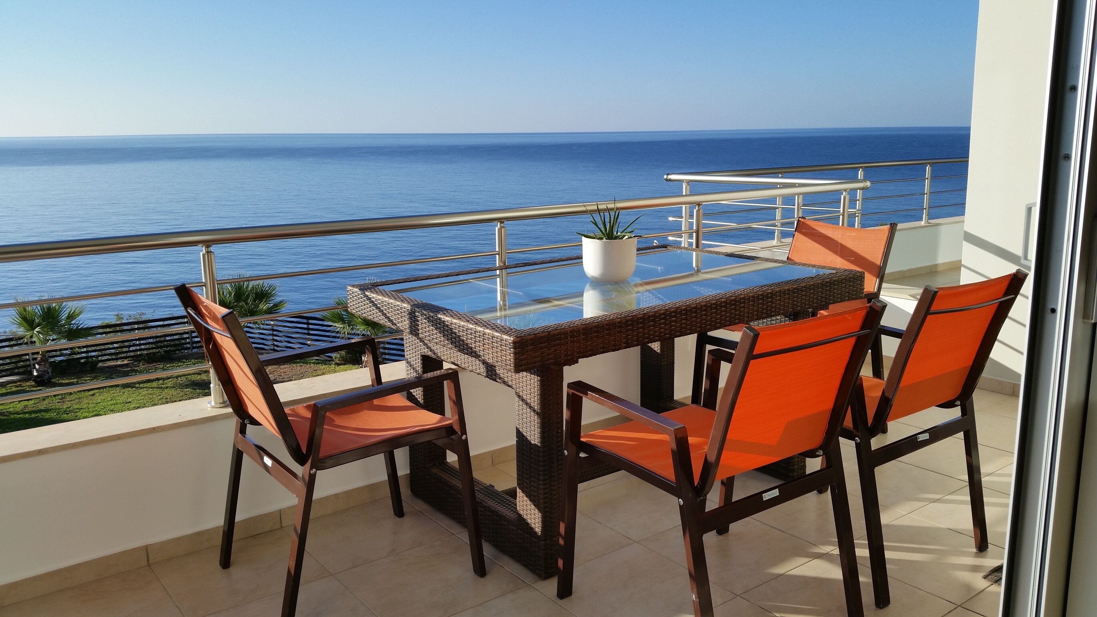 Un balcon avec une table et des chaises en verre, donnant sur la mer.