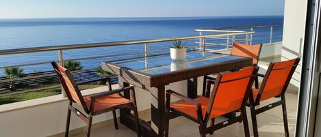 A balcony with a glass table and chairs, overlooking the sea.