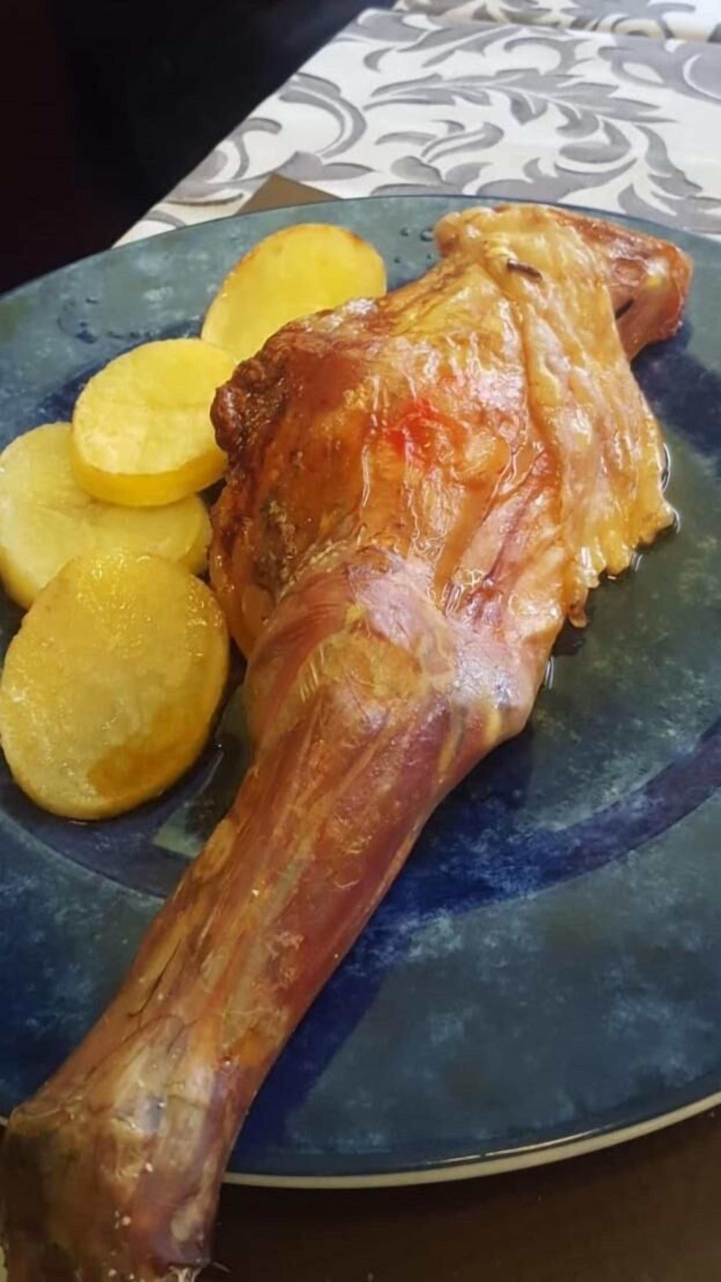 Pierna de cordero asada con patatas en un plato azul.