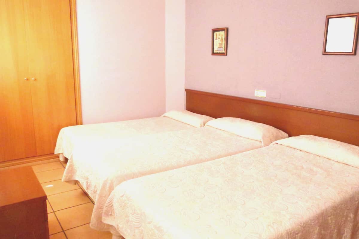 A room with two beds, a wooden wardrobe, and a framed picture on the wall.