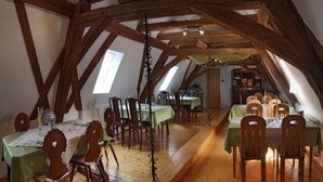 An attic dining area with wooden beams, green tablecloths, and wooden chairs. - Wörners Schloss Weingut & Wellness Hotel (Prichsenstadt)