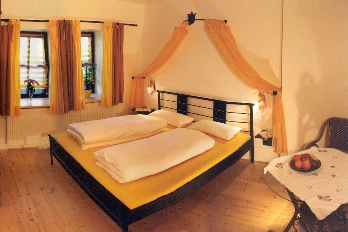 A single bed with a canopy, a bedside table with a fruit bowl, and a chair.