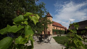 A courtyard with a building featuring a tower, surrounded by greenery and a gravel path. - Wörners Schloss Weingut & Wellness Hotel (Prichsenstadt)
