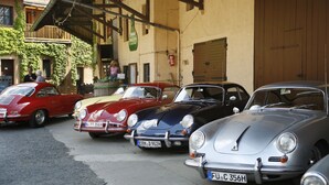 A row of vintage cars parked in front of a building with a wooden facade and a large garage door. - Wörners Schloss Weingut & Wellness Hotel (Prichsenstadt)