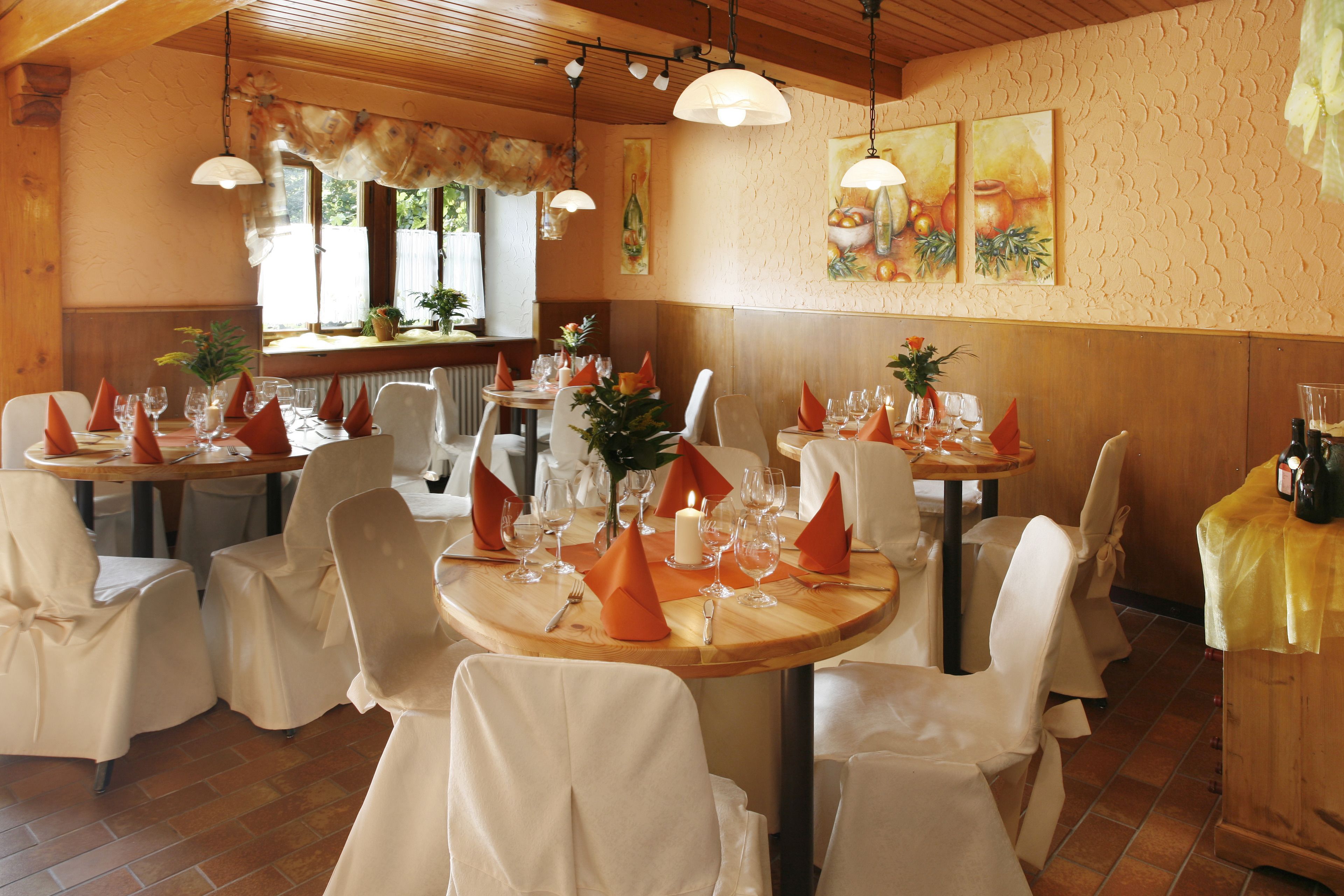 Ein Restaurant mit runden Tischen, weißen Stühlen und orangefarbenen Servietten.