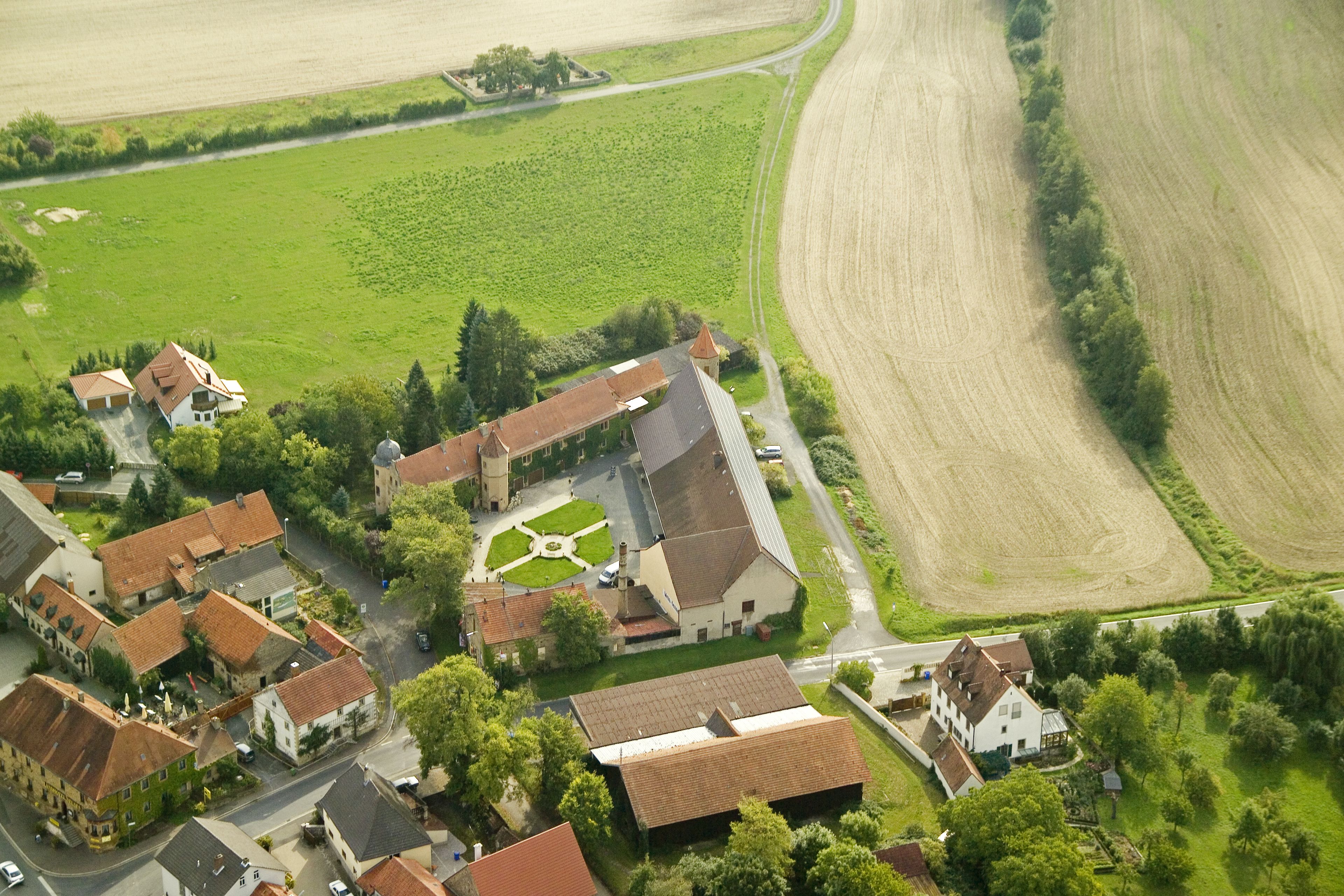 Luchtbeeld van een dorp met traditionele gebouwen, een kerk en omliggende landbouwvelden.