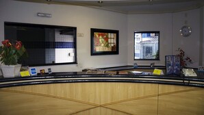A reception desk with a wooden finish, framed artwork above it, and a clock on the wall. - Omega Palace Hotel (São Paulo)