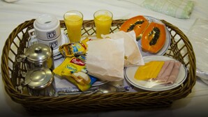 A breakfast tray with a coffee maker, two glasses of orange juice, a papaya, a plate of cheese and ham, and some snacks. - Omega Palace Hotel (São Paulo)