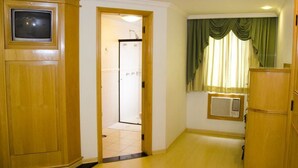 A room with wooden cabinets, a television, a bathroom with a shower, and a window with curtains. - Omega Palace Hotel (São Paulo)