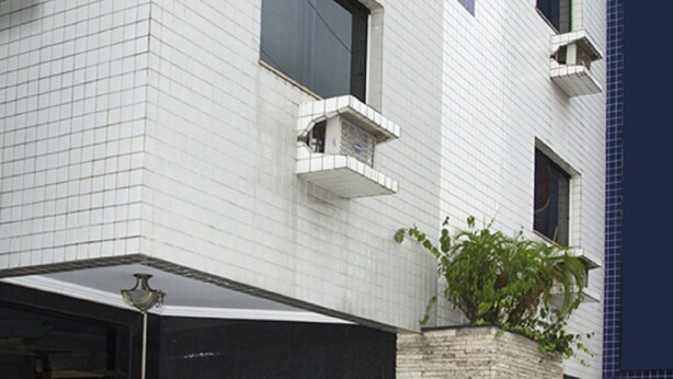 A modern building with a tiled facade, a small garden with plants, and a door with a doormat. - Omega Palace Hotel (São Paulo)