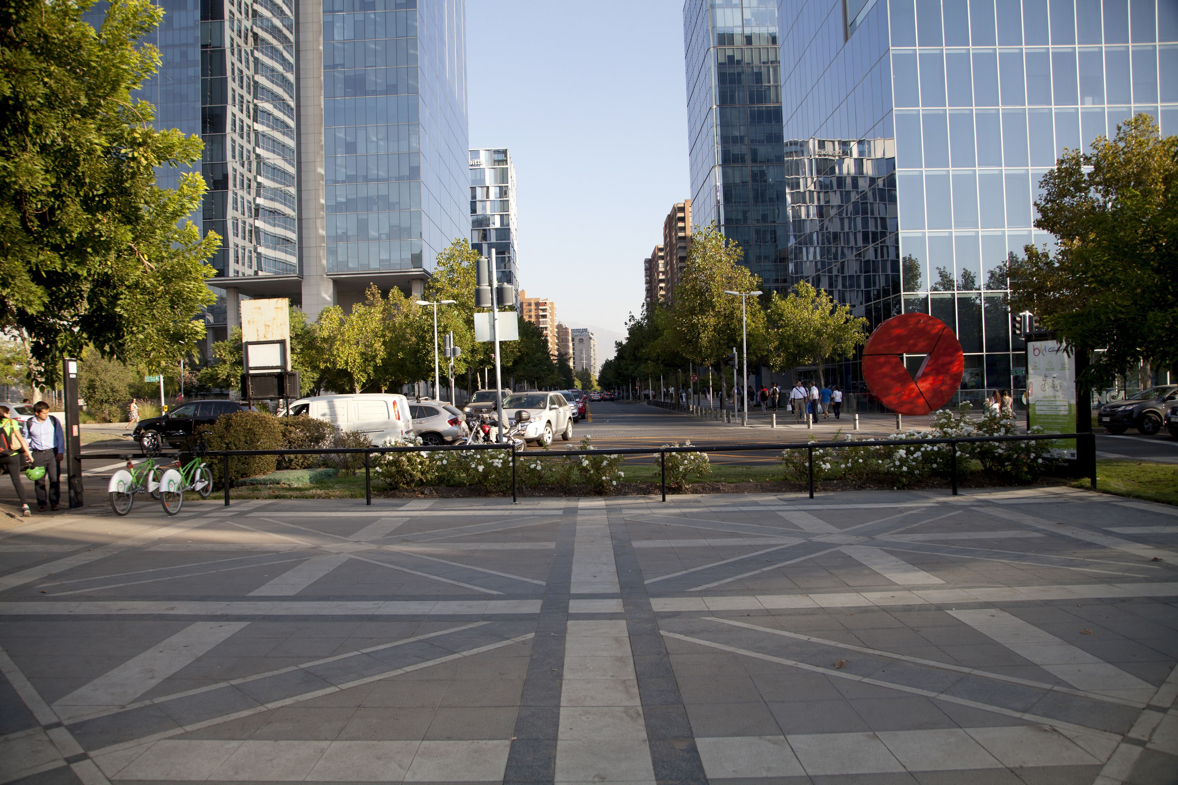 Una plaza urbana con edificios modernos, una gran escultura roja y algunas bicicletas estacionadas.