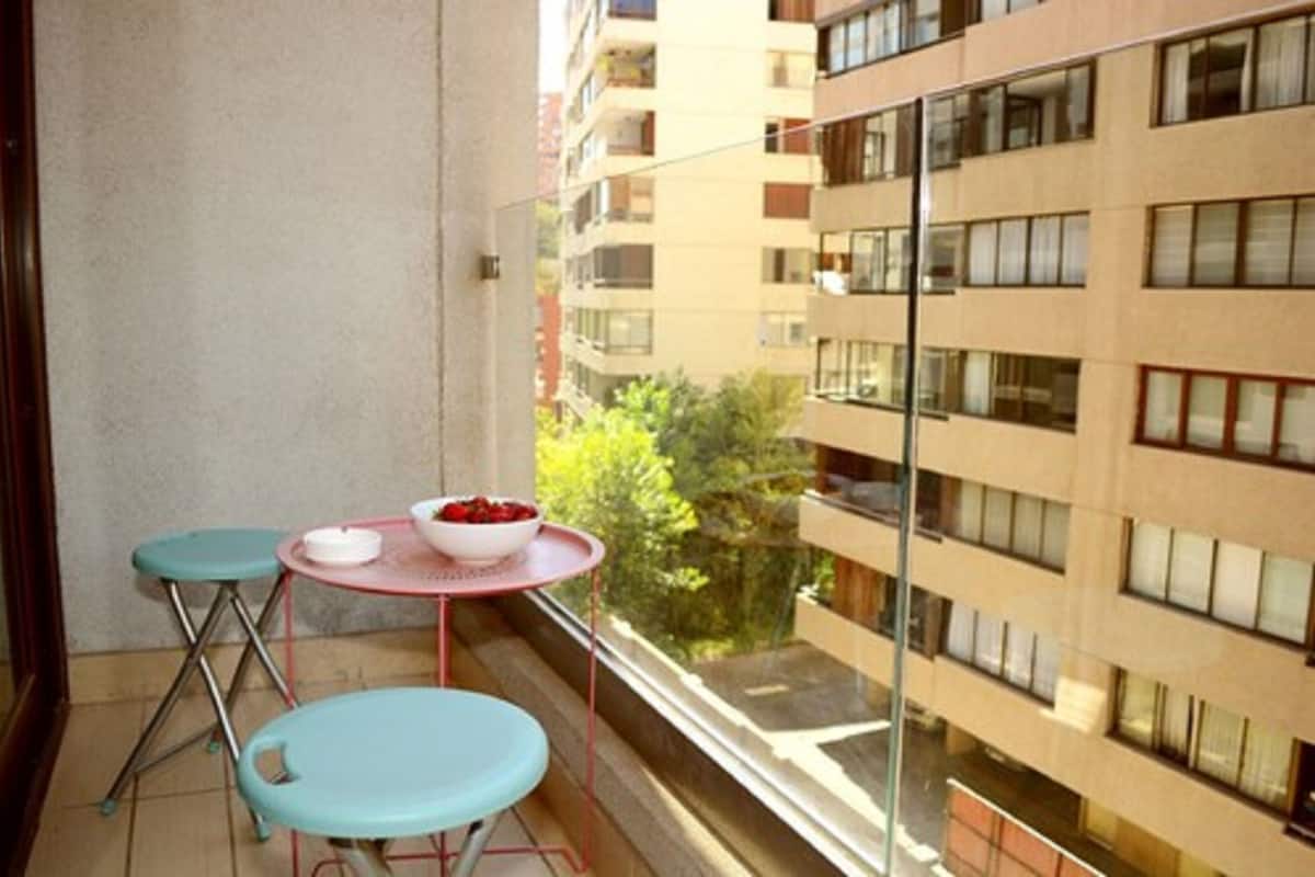 Un balcón con dos sillas y una mesita, con vista a un edificio con varias ventanas.