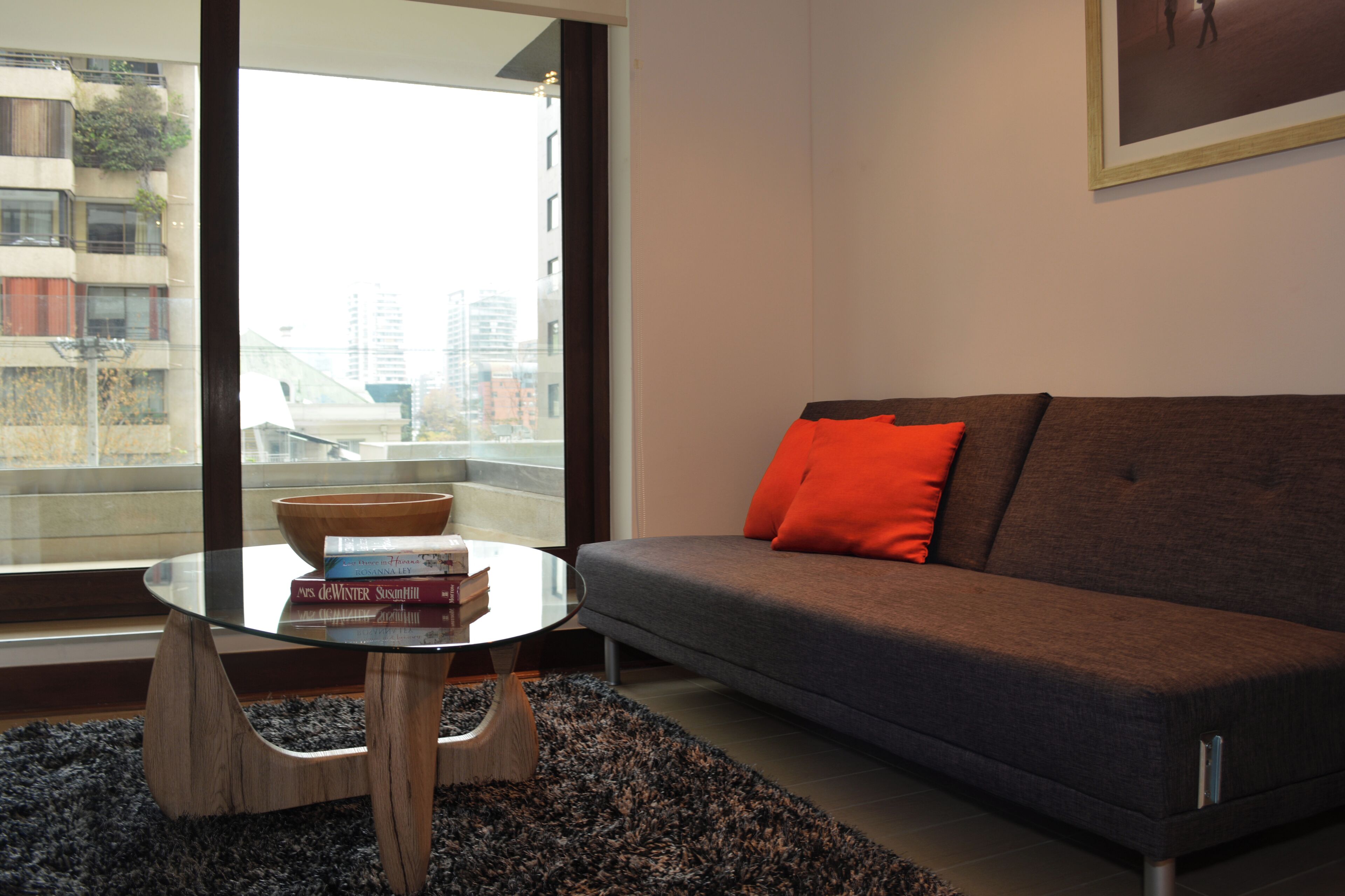 A modern living room with a sofa, a glass coffee table, and a view of a cityscape through large windows.