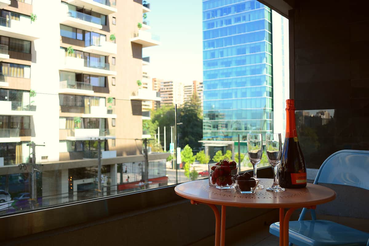 Un balcón con una mesa preparada para dos personas, con una botella de vino, dos copas y un vaso con fresas.