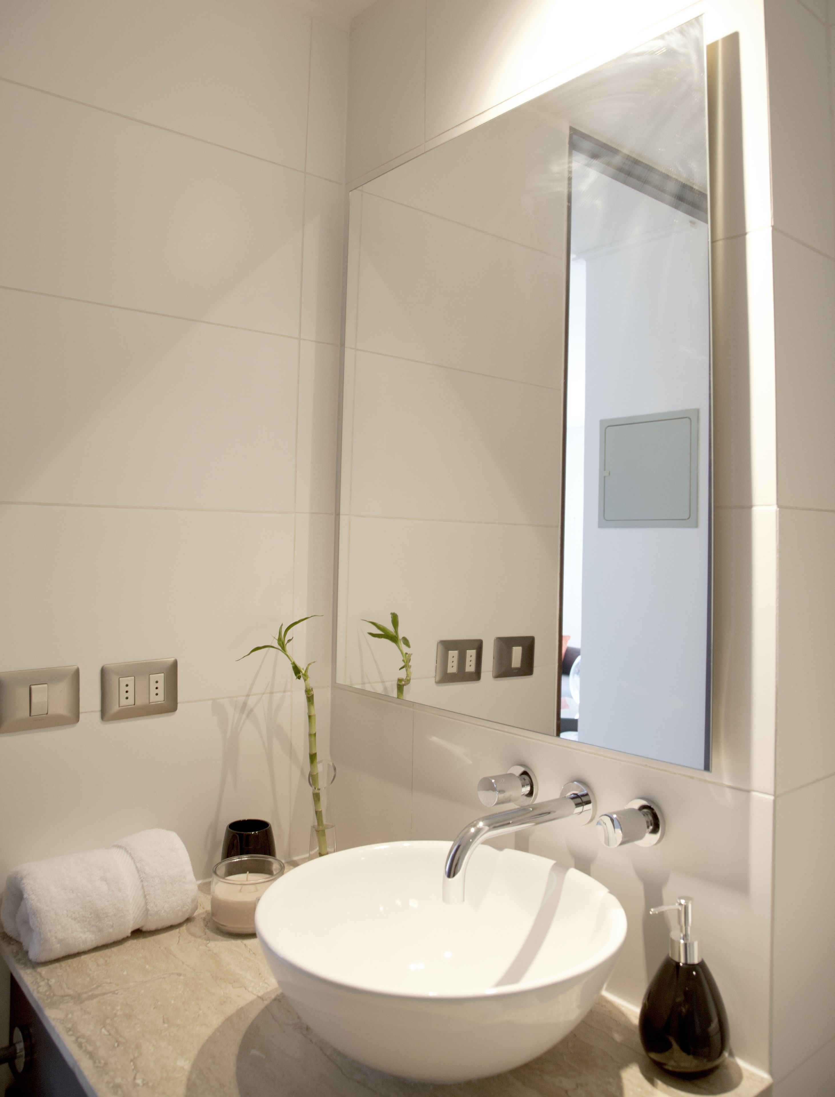 A modern bathroom with a large mirror, a white sink, a towel, and a small plant.